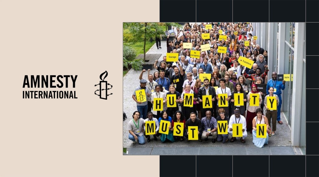 A large group holds yellow signs reading Humanity Must Win at an Amnesty International event, featured on the Amnesty WordPress blog.