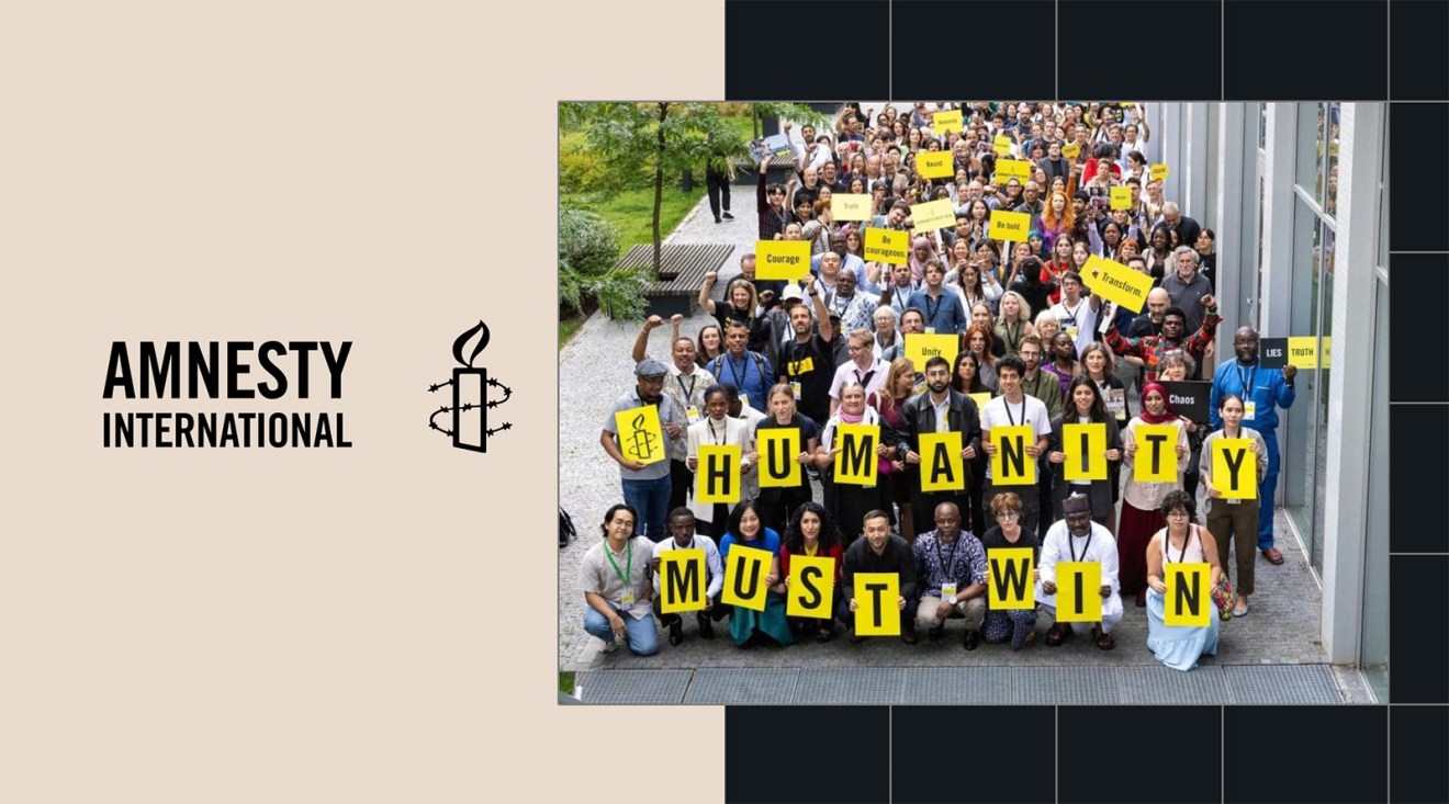 A large group holds yellow signs reading Humanity Must Win at an Amnesty International event.