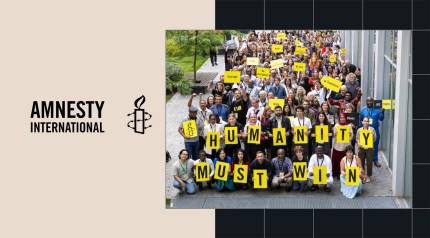A large group holds yellow signs reading Humanity Must Win at an Amnesty International event.