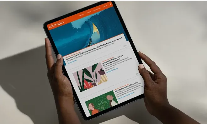 Person holding a tablet displaying the Edutopia homepage with featured education articles and colorful illustrations.