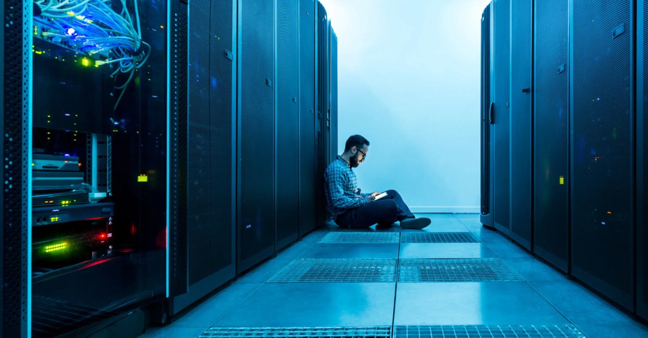 a person sitting in a server room looking down at their phone