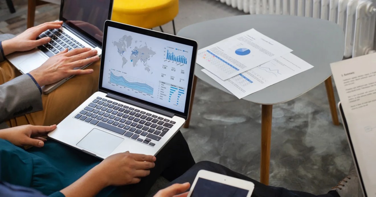 An image of a several people collaborating, two using laptops to look at location metrics, while one looks at a table, and another reviews a printed document.