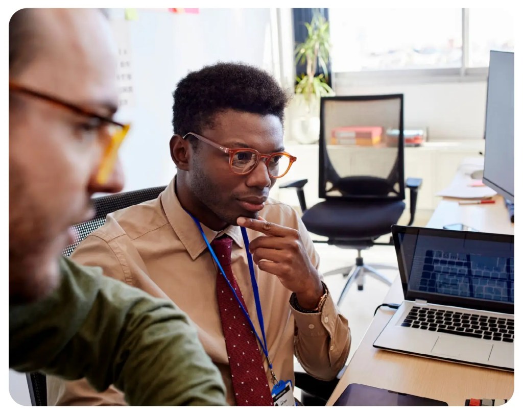 Two people review digital solution content on a laptop, one considering editorial workflow decisions.