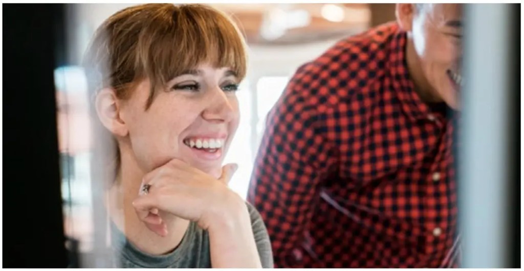 Smiling woman reviews content with colleague on a digital solution dashboard.