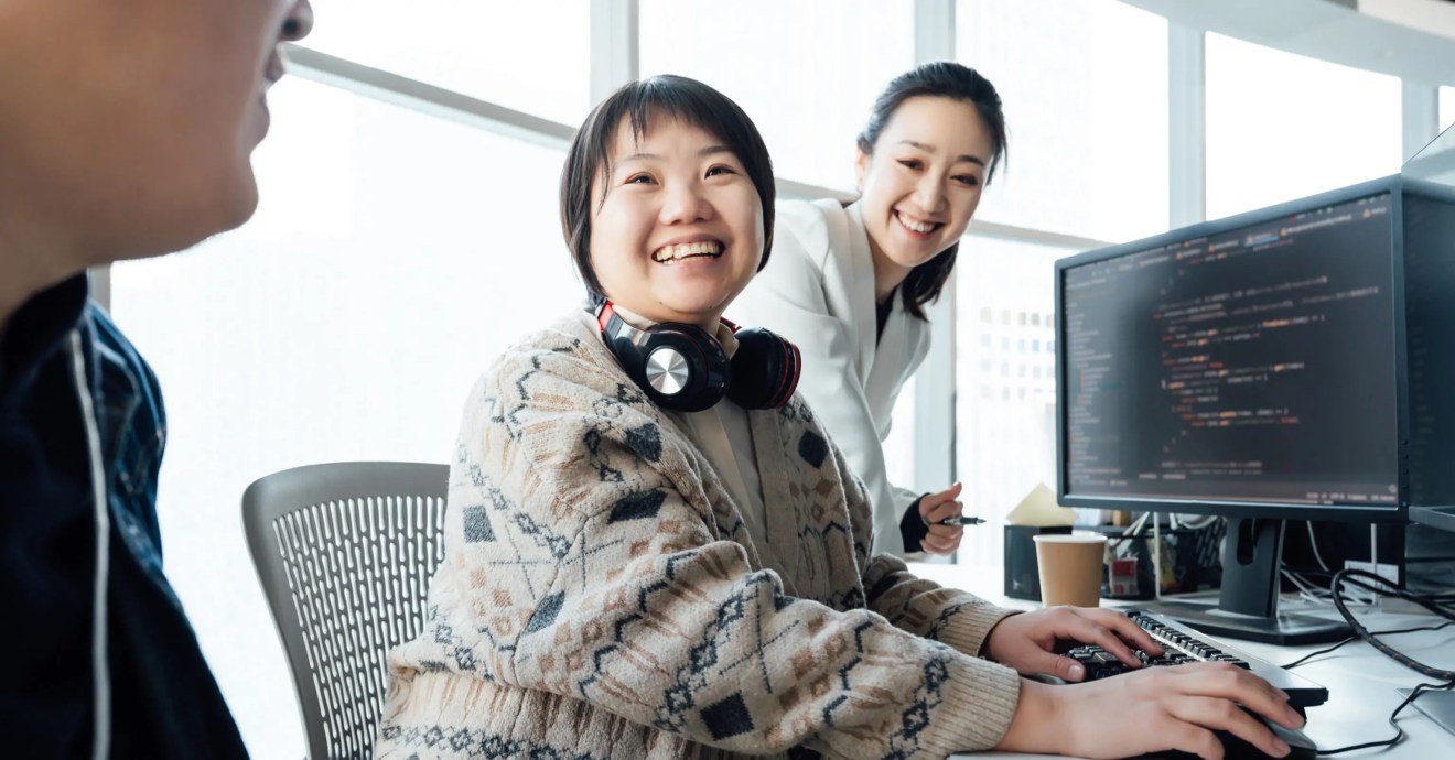 Two women collaborating at a computer on digital solution code for content or workflow development.