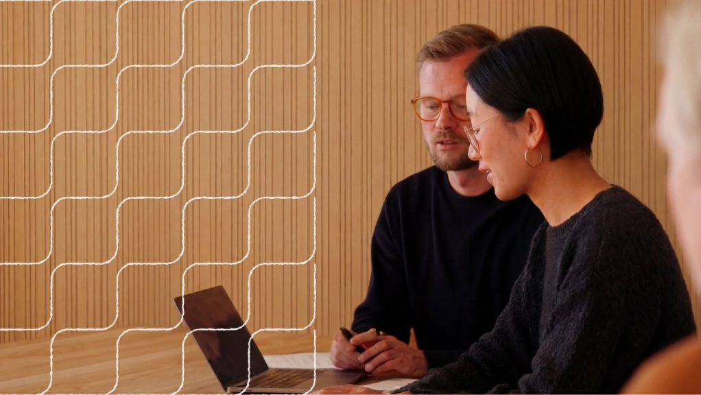 Two people seated at a table, looking at a laptop in a wood-paneled meeting room.