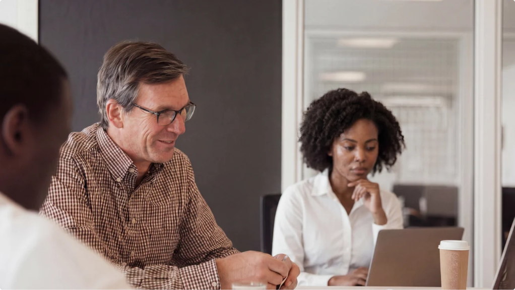 Team members meeting around a conference table with laptops.
