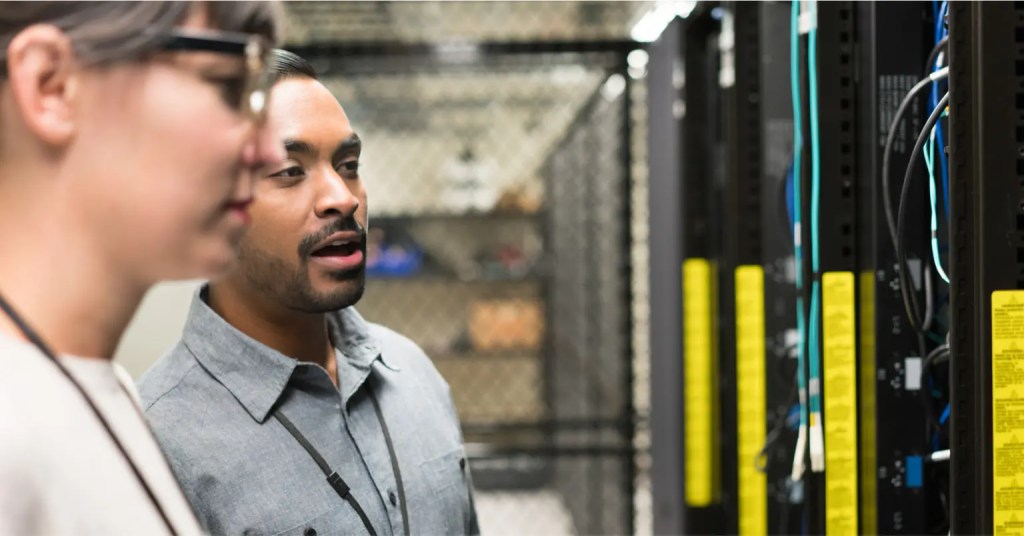 Two people review server racks, discussing networking cables and digital solution infrastructure performance.