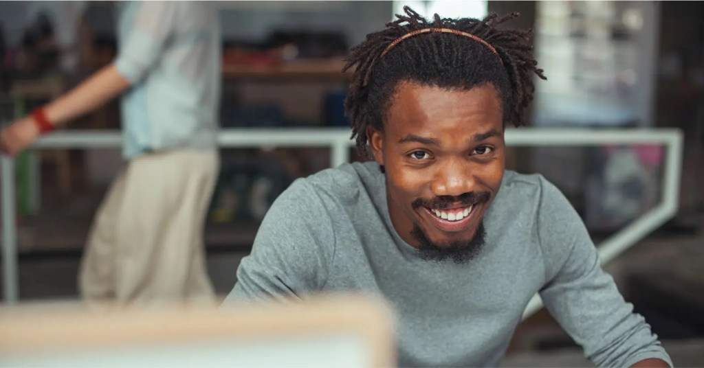 Smiling man with dreadlocks and beard using digital solution content dashboard, facing the camera.