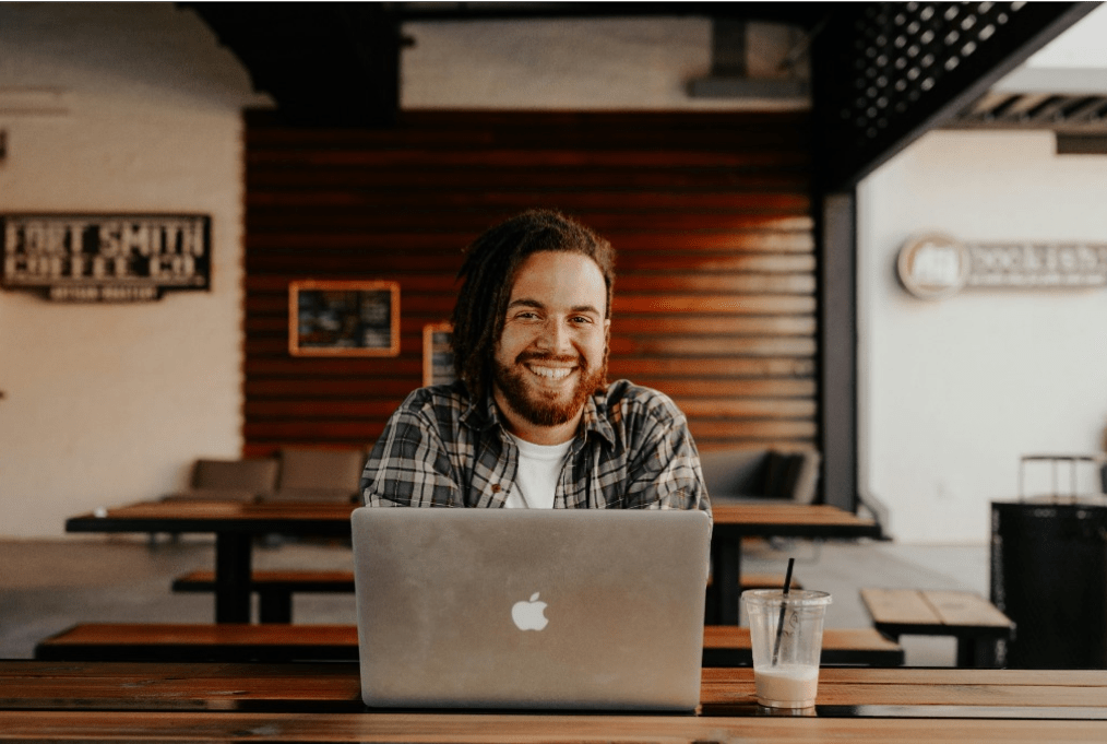 Smiling man with dreadlocks works on laptop in a digital solution content or editorial workflow setting.
