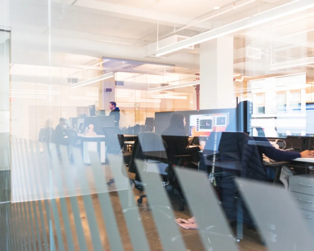 An open plan office space featuring people working at computer desks in a well lit room