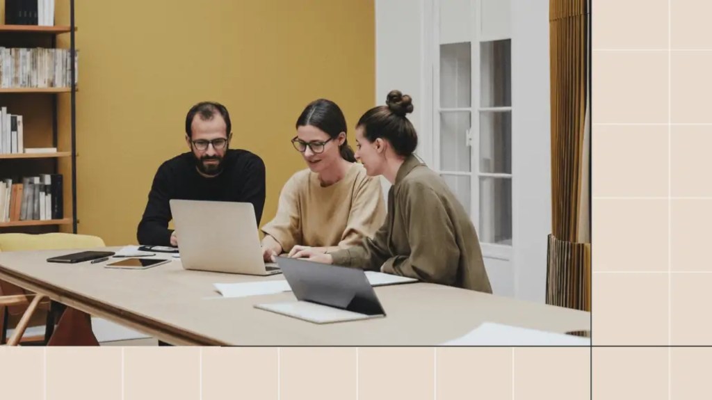 Three people collaborating at a table with laptops, reviewing work together.