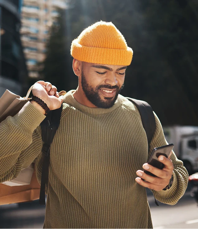 Person carrying shopping bags while looking at a smartphone outdoors.