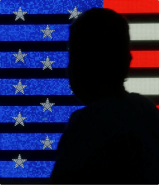 Silhouette of a person standing in front of a digital display showing the United States flag.