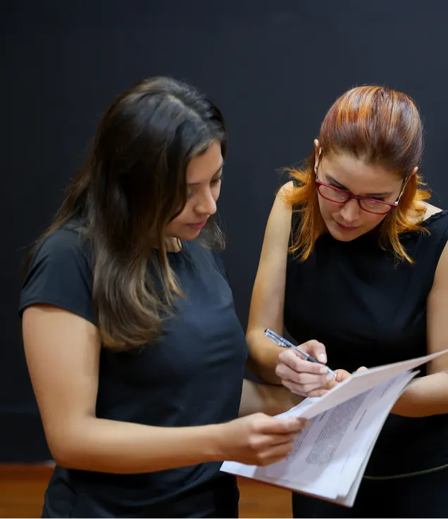 Two colleagues reviewing a printed document together, with one person making notes while the other holds the pages.