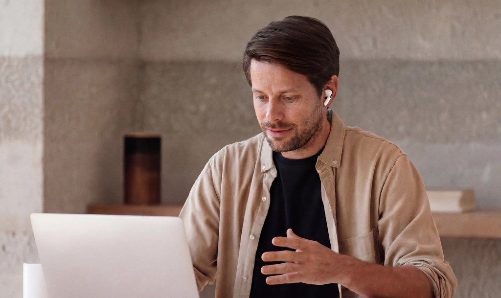 Person wearing wireless earbuds while participating in a video call on a laptop.