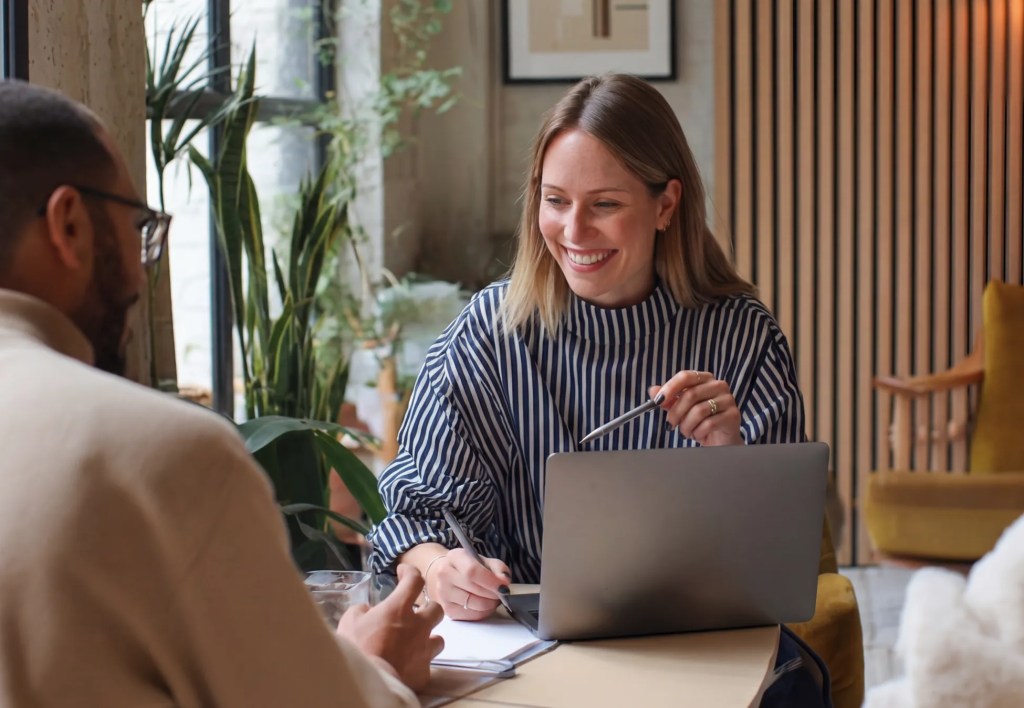 Two colleagues discussing ideas over a laptop during a planning meeting using a CMS for marketers.