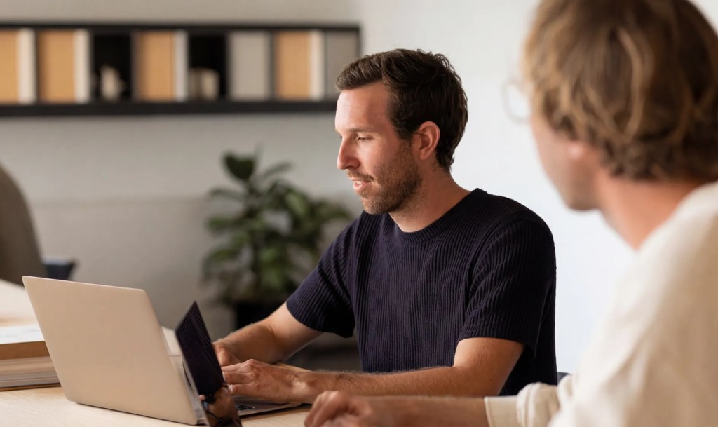 Team members collaborating around a laptop while discussing a SaaS CMS content and development workflow.