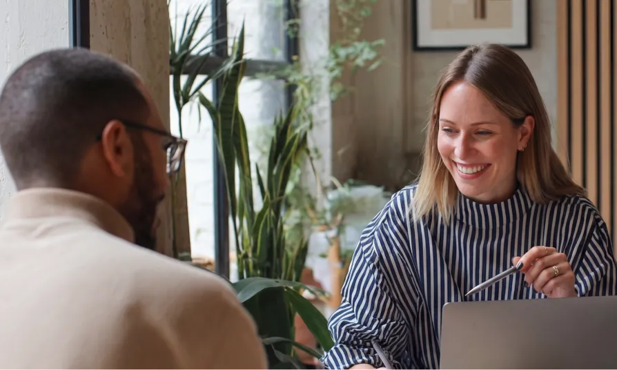 Two colleagues discussing ideas over a laptop during a planning meeting using a CMS for marketers.
