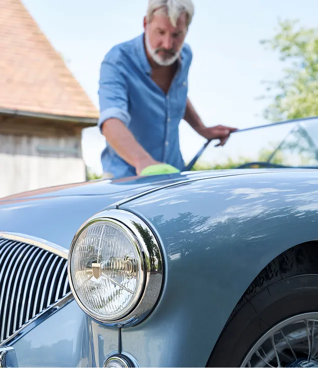 Close-up of a vintage car while a person polishes the hood.