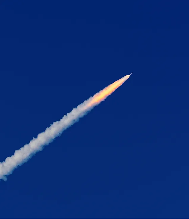 Rocket launching into a clear blue sky with a bright exhaust plume and white smoke trail.