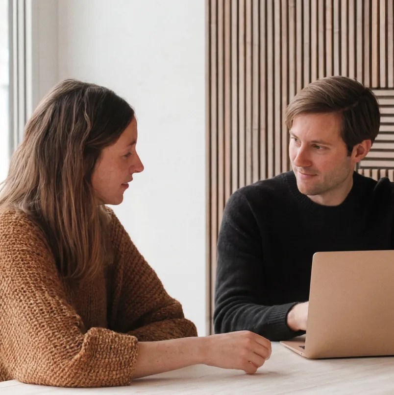 Two colleagues discussing a project while reviewing work on a laptop at a meeting table.