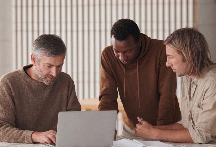 Three men working together at a table, looking at a laptop with papers and a pen in hand, as they discuss solutions tailored for WordPress VIP for enterprise brands.