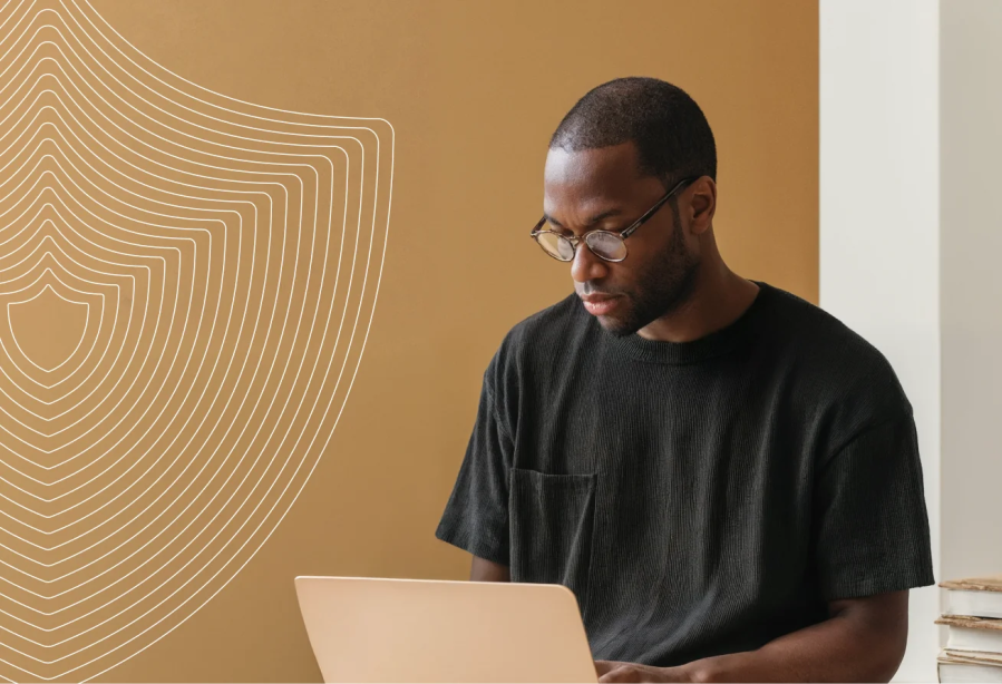 Man wearing glasses uses a laptop, sitting by a brown wall with abstract white lines and shield shapes—an ideal setting for exploring how WordPress VIP for enterprise brands empowers large companies with secure, scalable digital solutions.